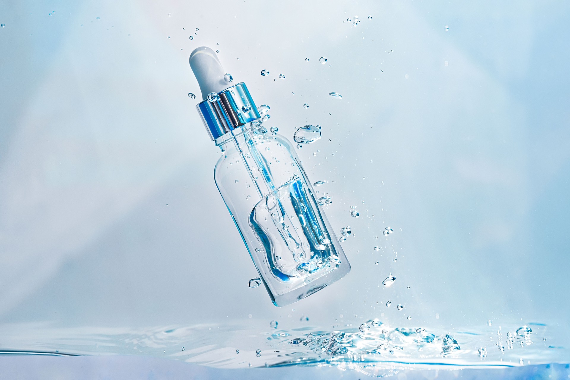 Cosmetic essence in glass bottle with pipette in transparent water with bubbles
